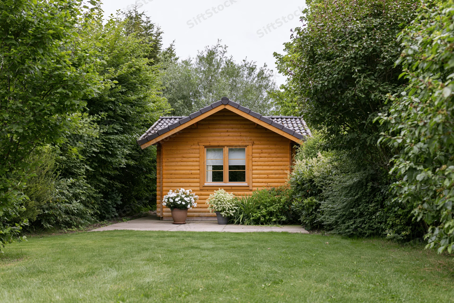 Small wooden cabin with tiled roof surrounded by greenery in a garden setting