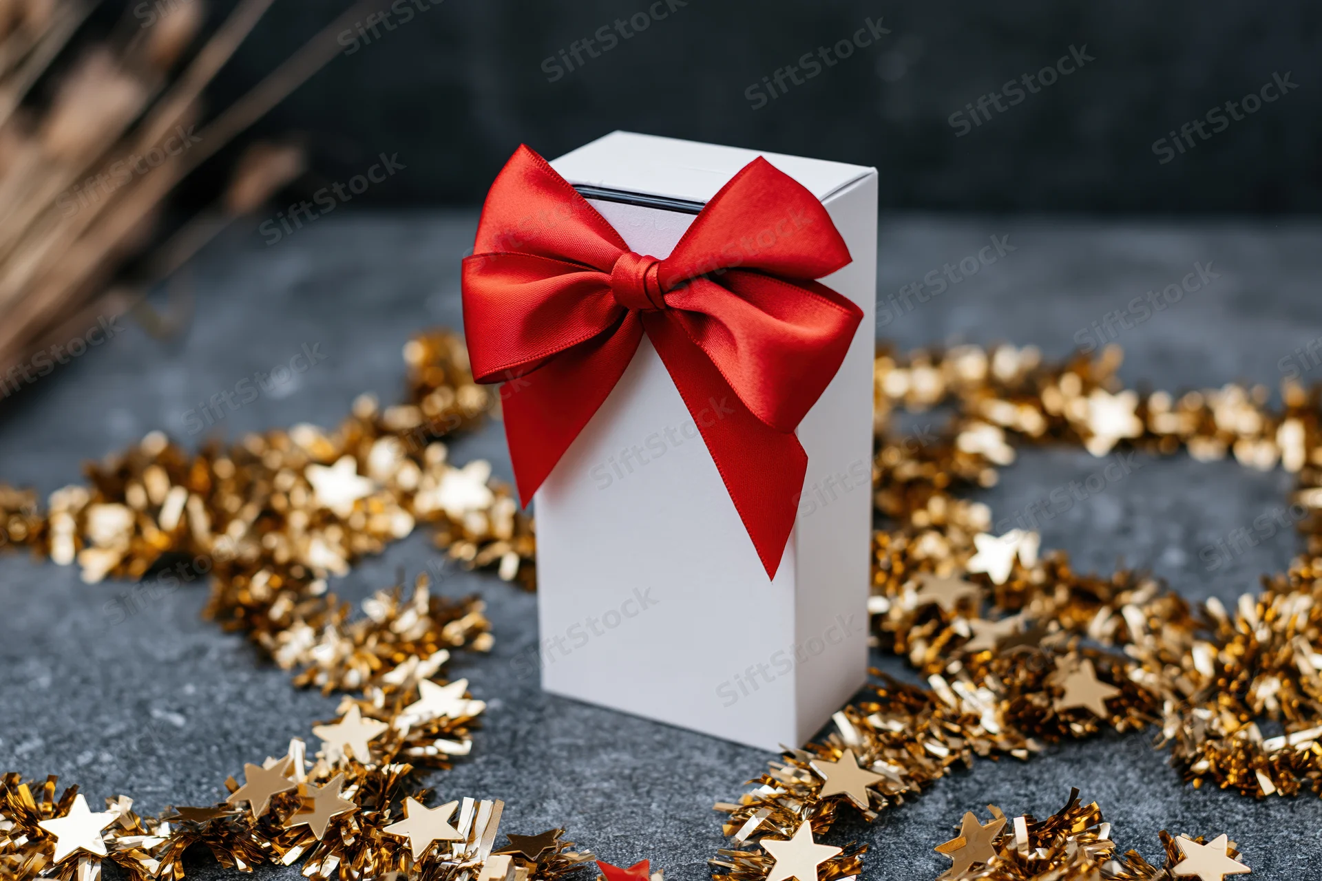 White gift box with red bow and gold star tinsel on dark surface
