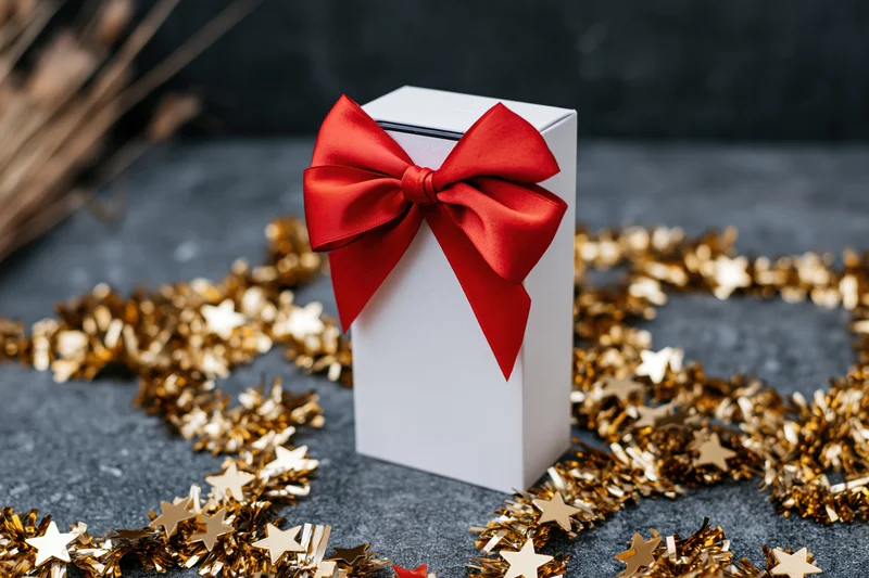White gift box with red bow and gold star tinsel on dark surface