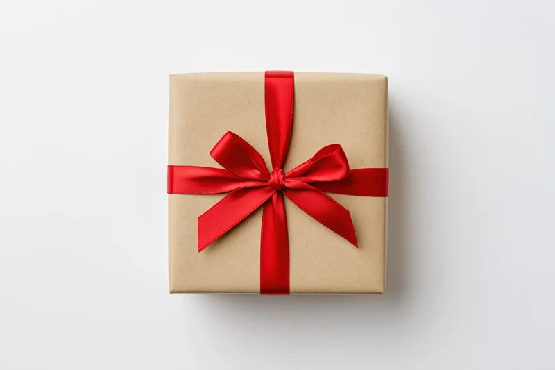 Square gift box wrapped in kraft paper with red ribbon bow on white background