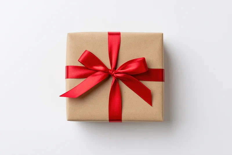 Square gift box wrapped in kraft paper with red ribbon bow on white background