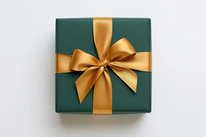 Square gift box wrapped in matte dark green paper with gold ribbon bow on white background
