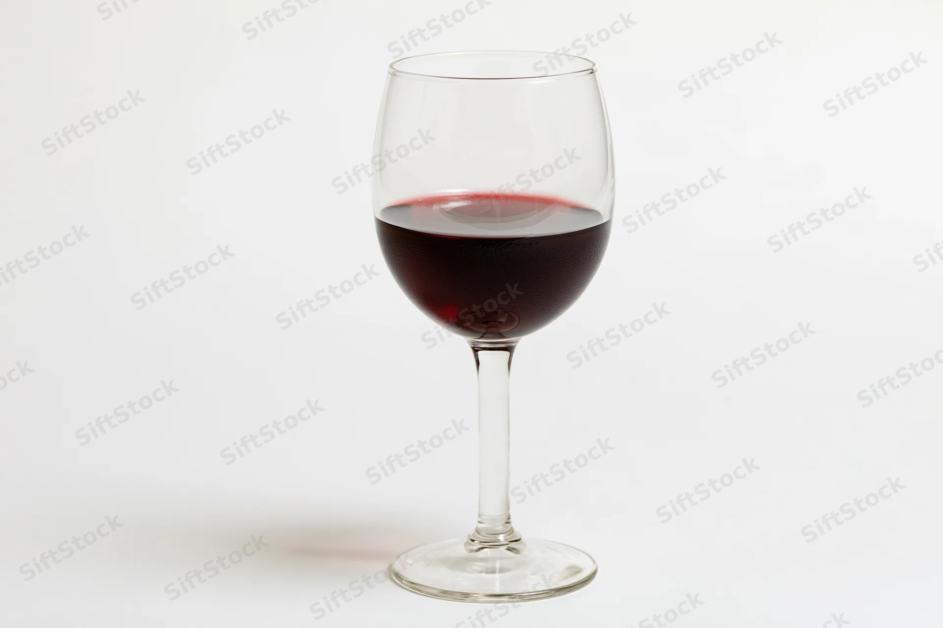 Stemmed wine glass half-filled with deep red wine centered on white background