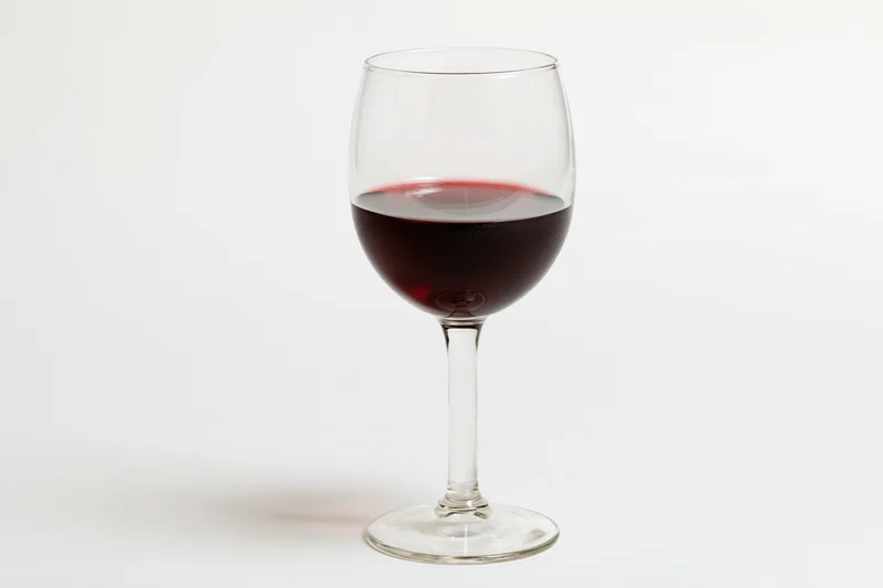 Stemmed wine glass half-filled with deep red wine centered on white background