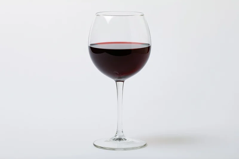 A stemmed wine glass half-filled with deep red wine centered on a white background