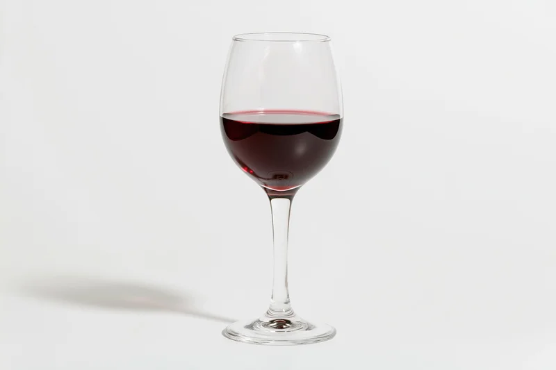 A stemmed wine glass half-filled with deep red wine centered on a white surface