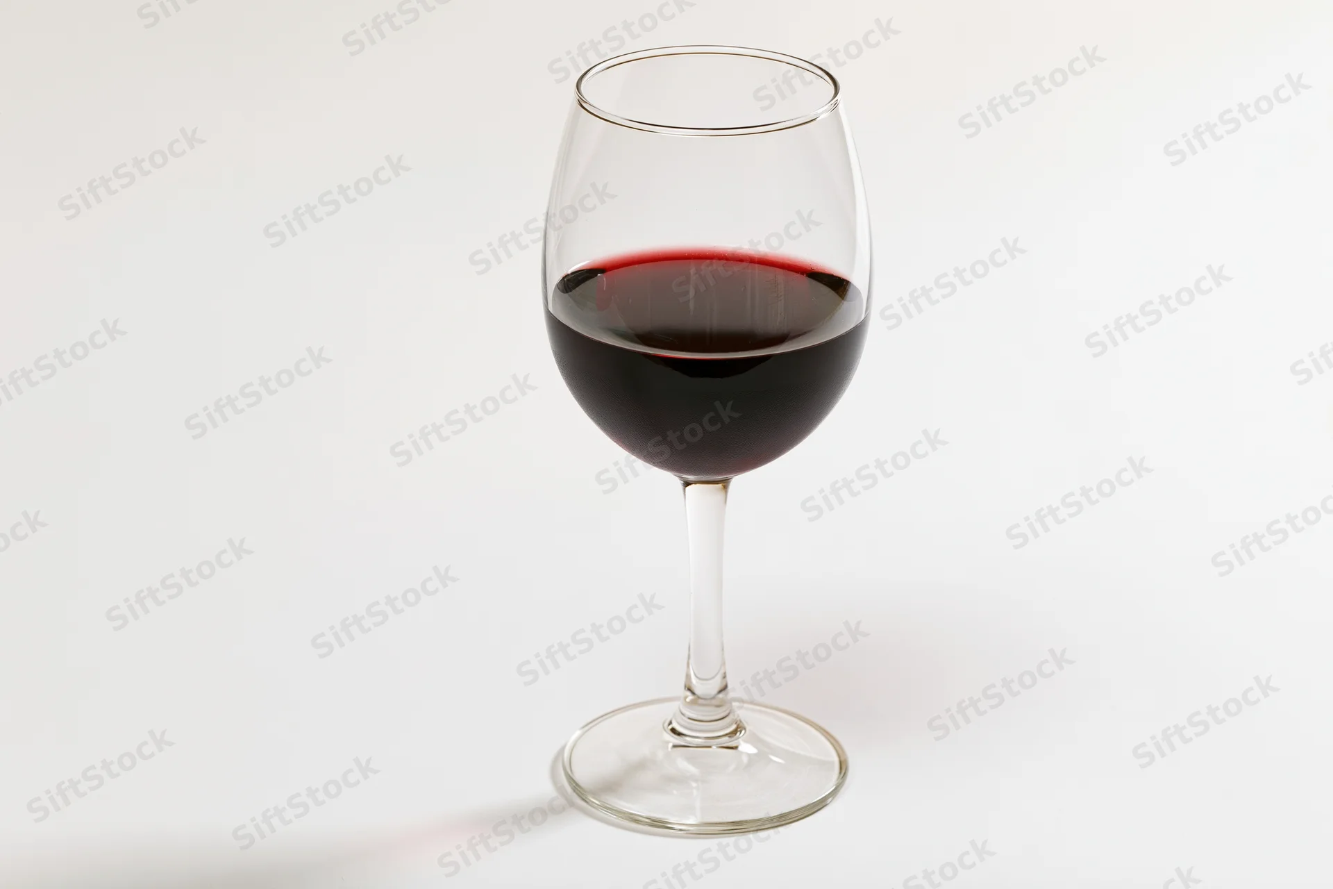 Stemmed wine glass half-filled with deep red wine centered on white background