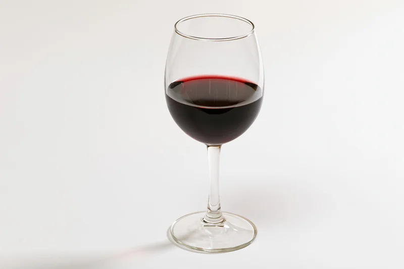 Stemmed wine glass half-filled with deep red wine centered on white background