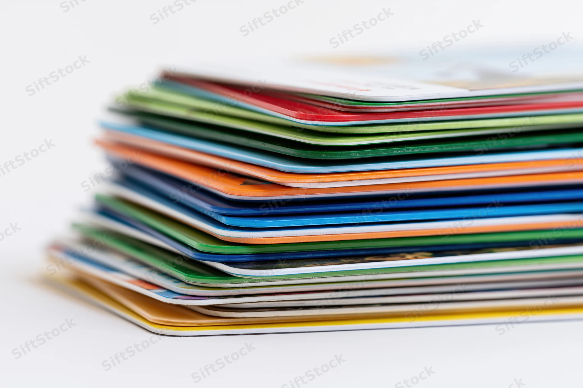Tall stack of colorful plastic credit cards piled unevenly on white background