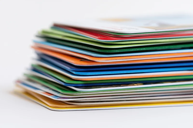 Tall stack of colorful plastic credit cards piled unevenly on white background