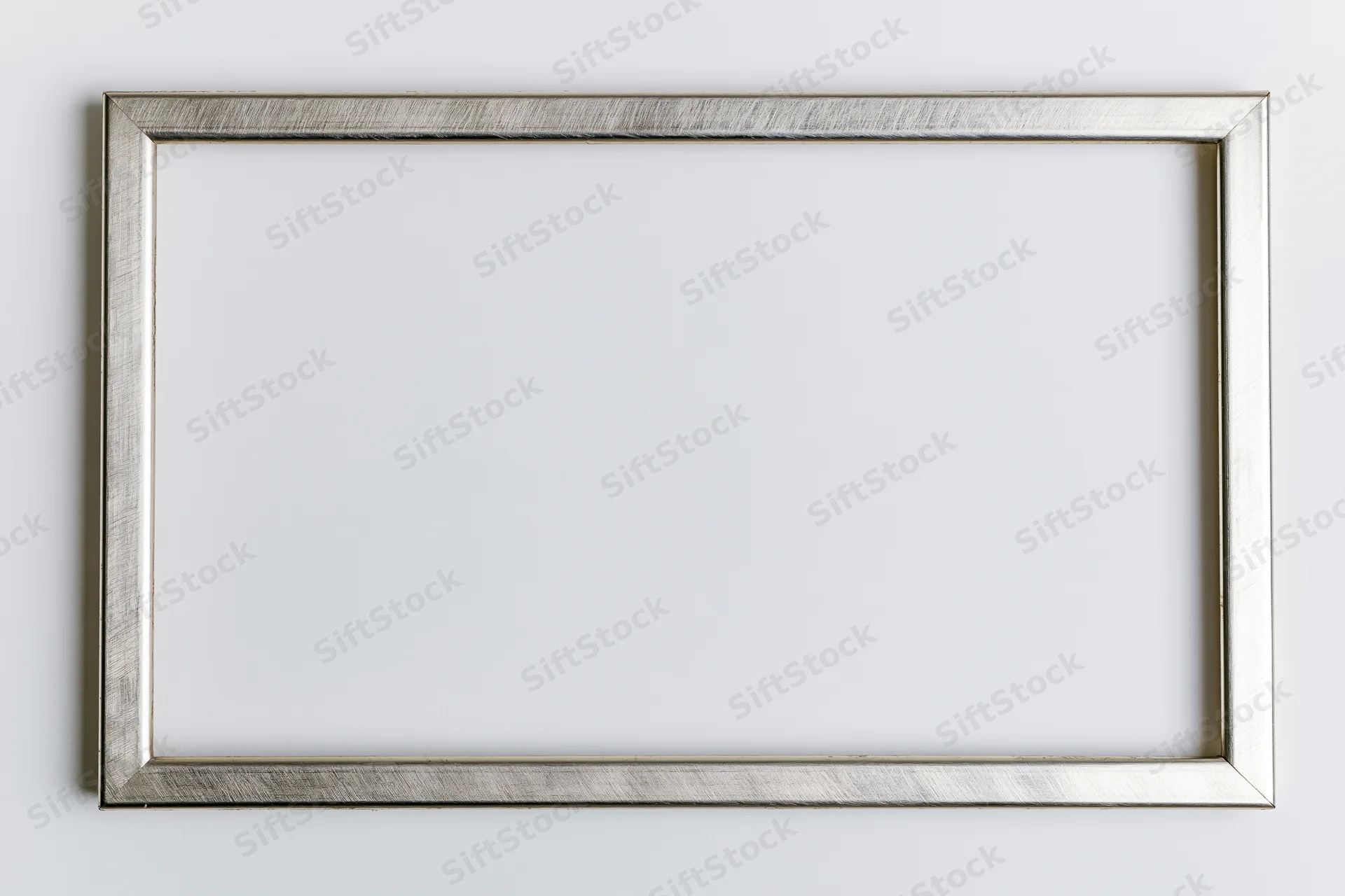Silver metallic picture frame hanging on white wall with empty space for artwork