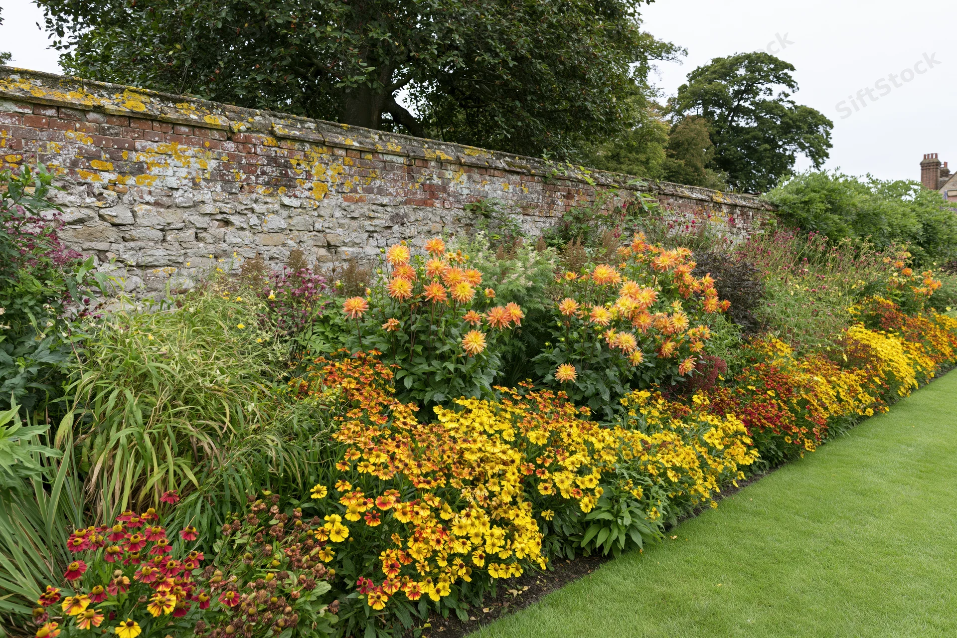 Colorful flowerbed along a brick and stone garden wall beside a lawn