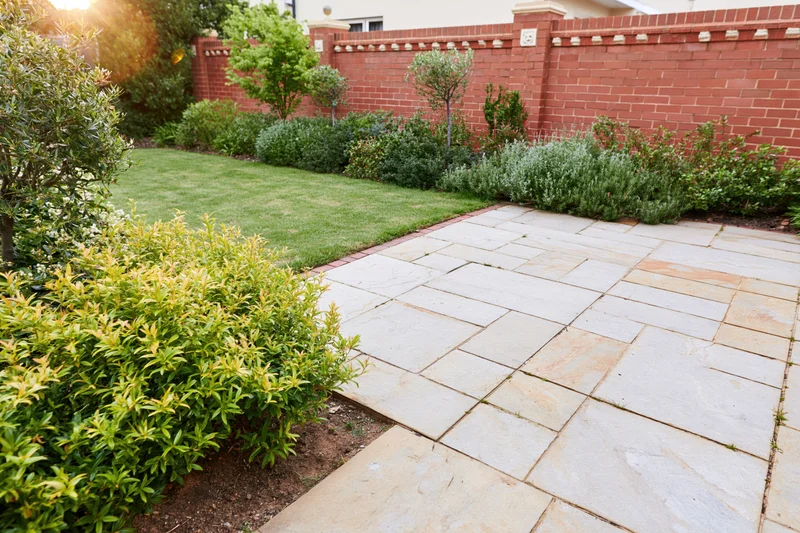 Stone paver patio surrounded by green shrubs and lawn in a backyard garden