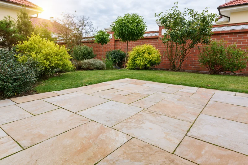 Stone paver patio in a landscaped backyard garden with shrubs and brick wall