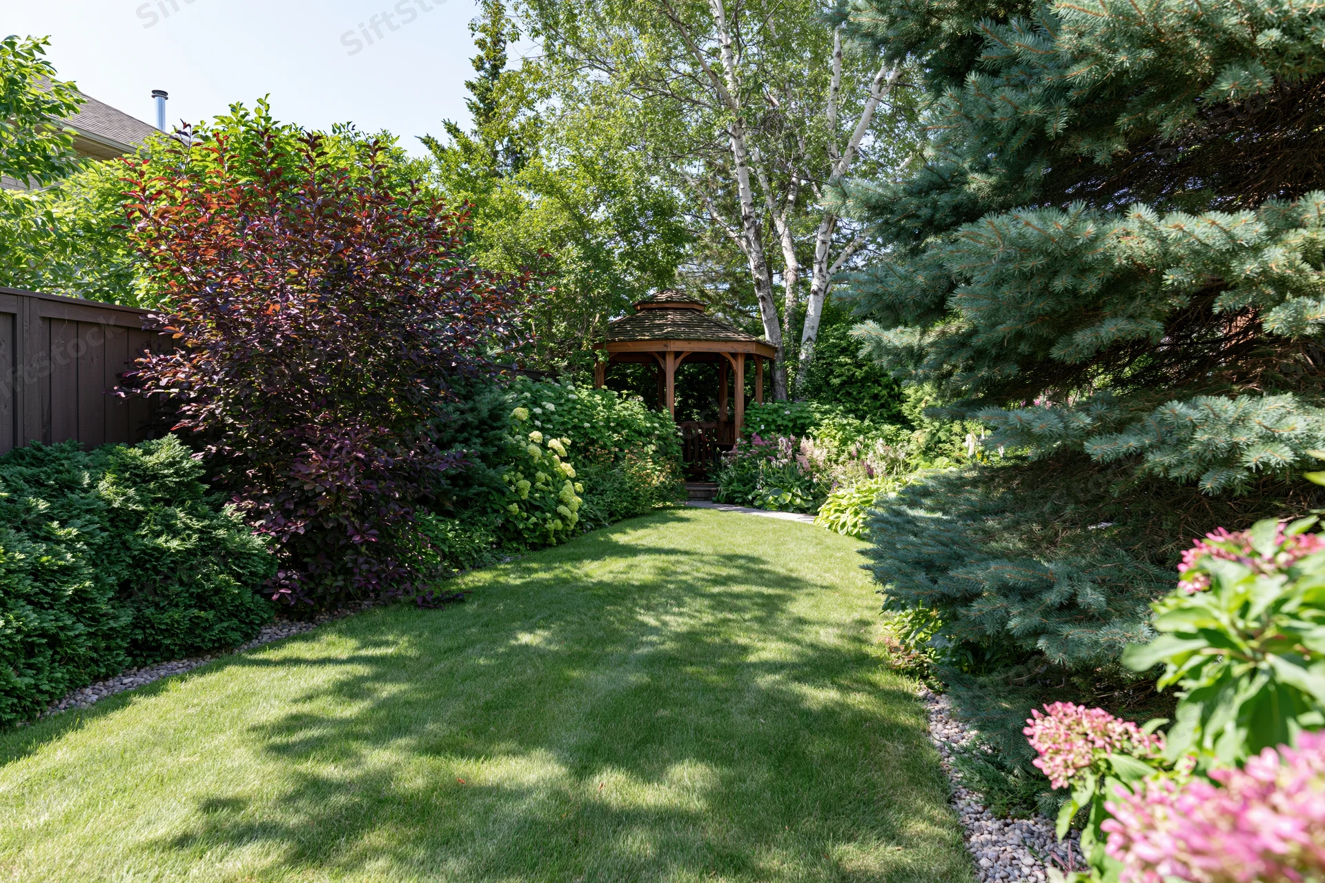 Narrow green lawn path leading to wooden gazebo in private backyard garden surrounded by shrubs and trees
