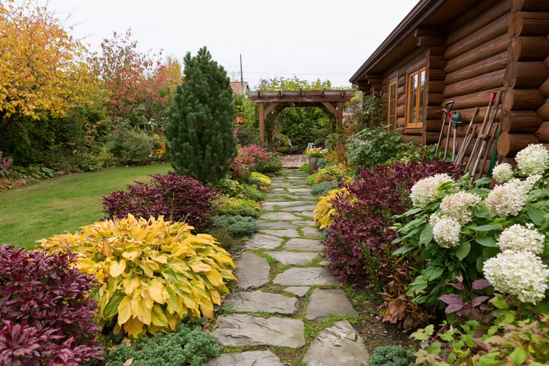 Stone path winding through colorful autumn garden beside log cabin