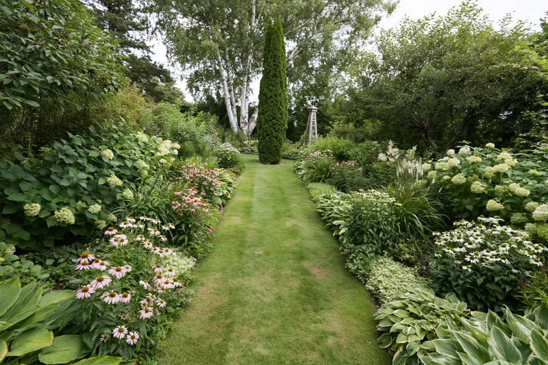 Grass path lined with flowering plants and shrubs in a private garden