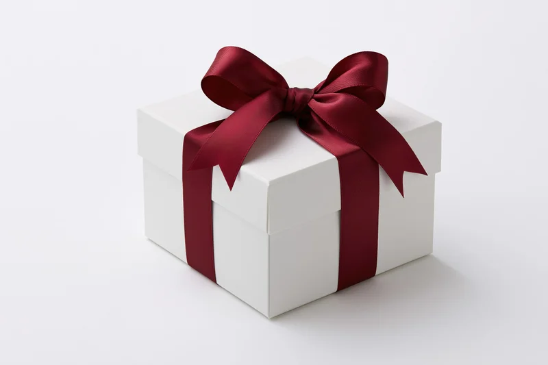 White gift box wrapped with red satin ribbon on plain white surface