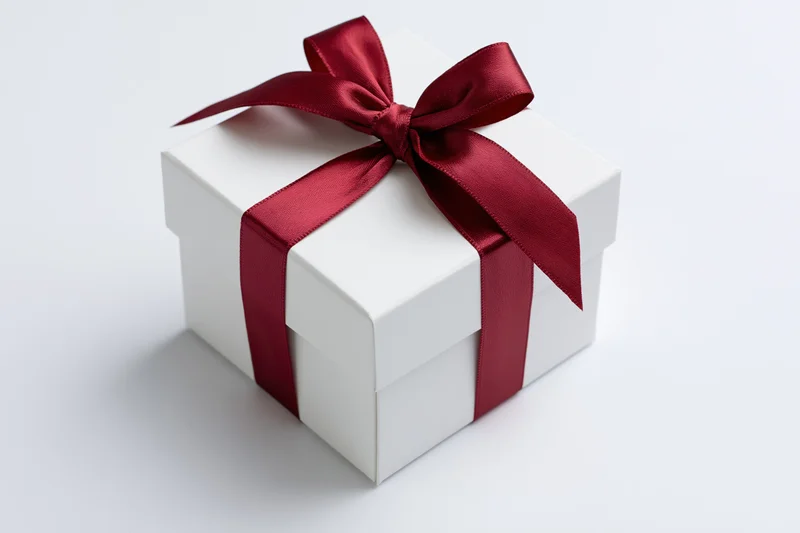 White gift box wrapped with red satin ribbon on plain white surface