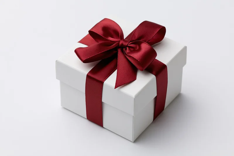 White gift box with red satin ribbon on plain white surface