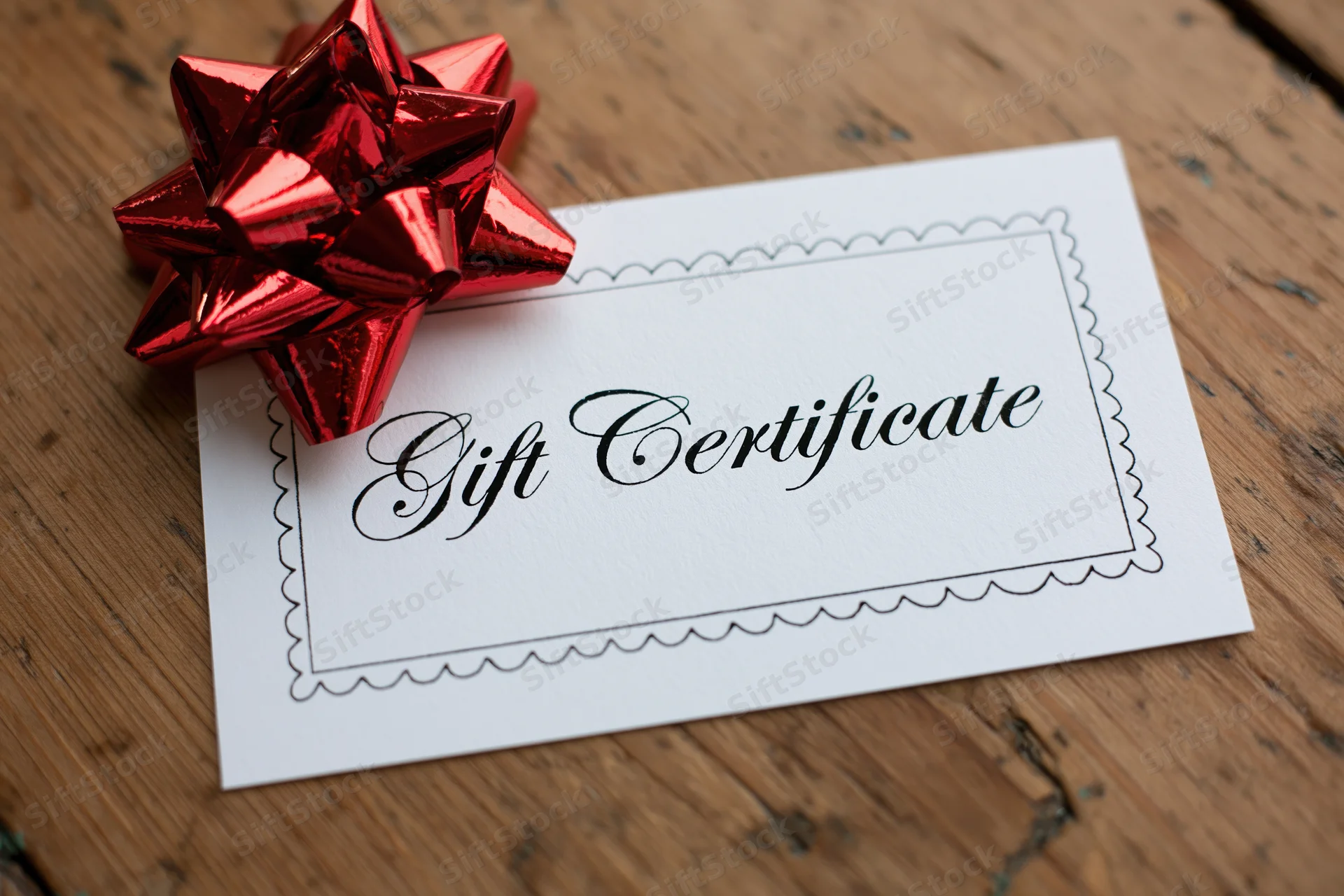 White gift certificate card with red foil bow on wooden surface