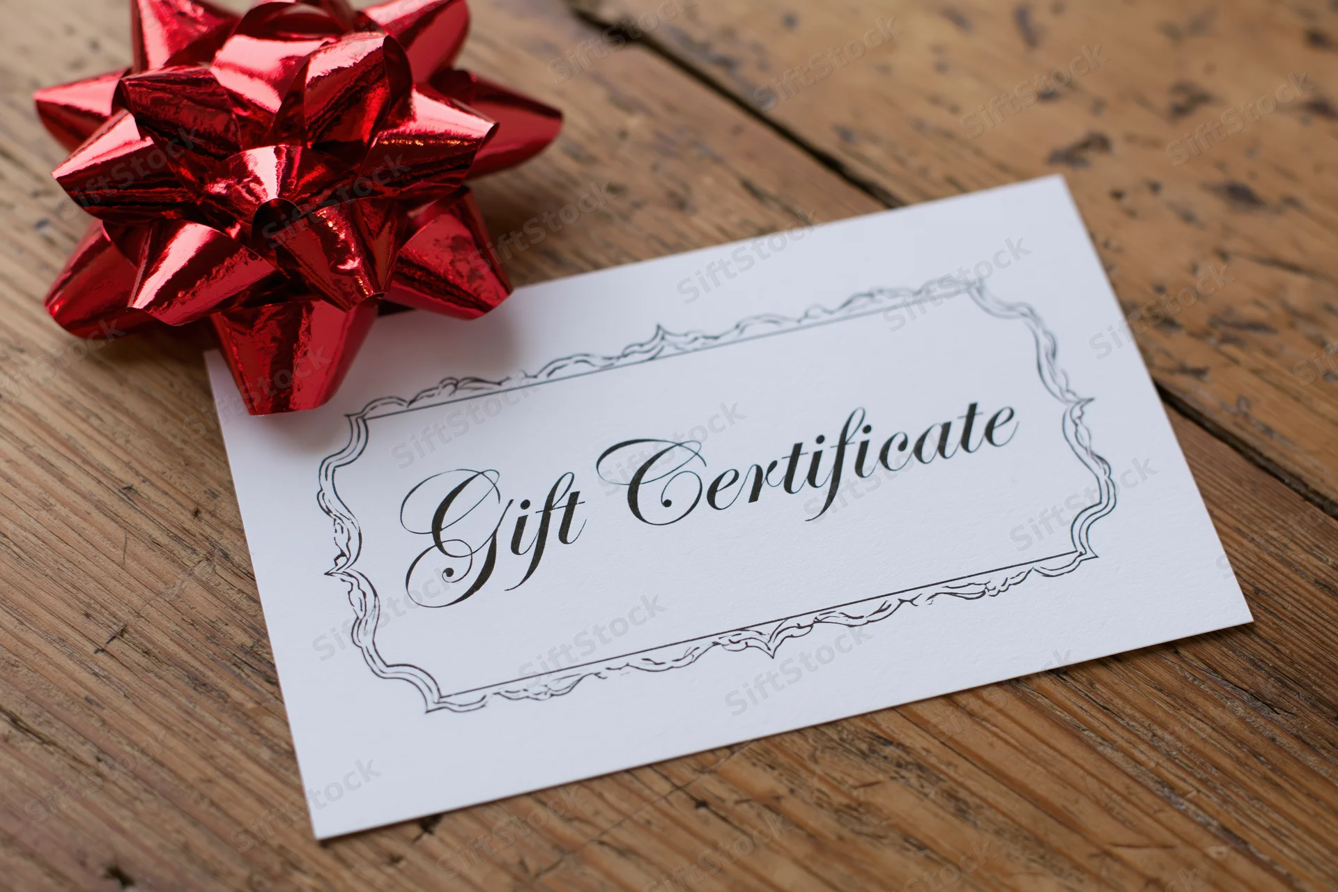White gift certificate card with decorative scalloped border and red bow on wooden surface