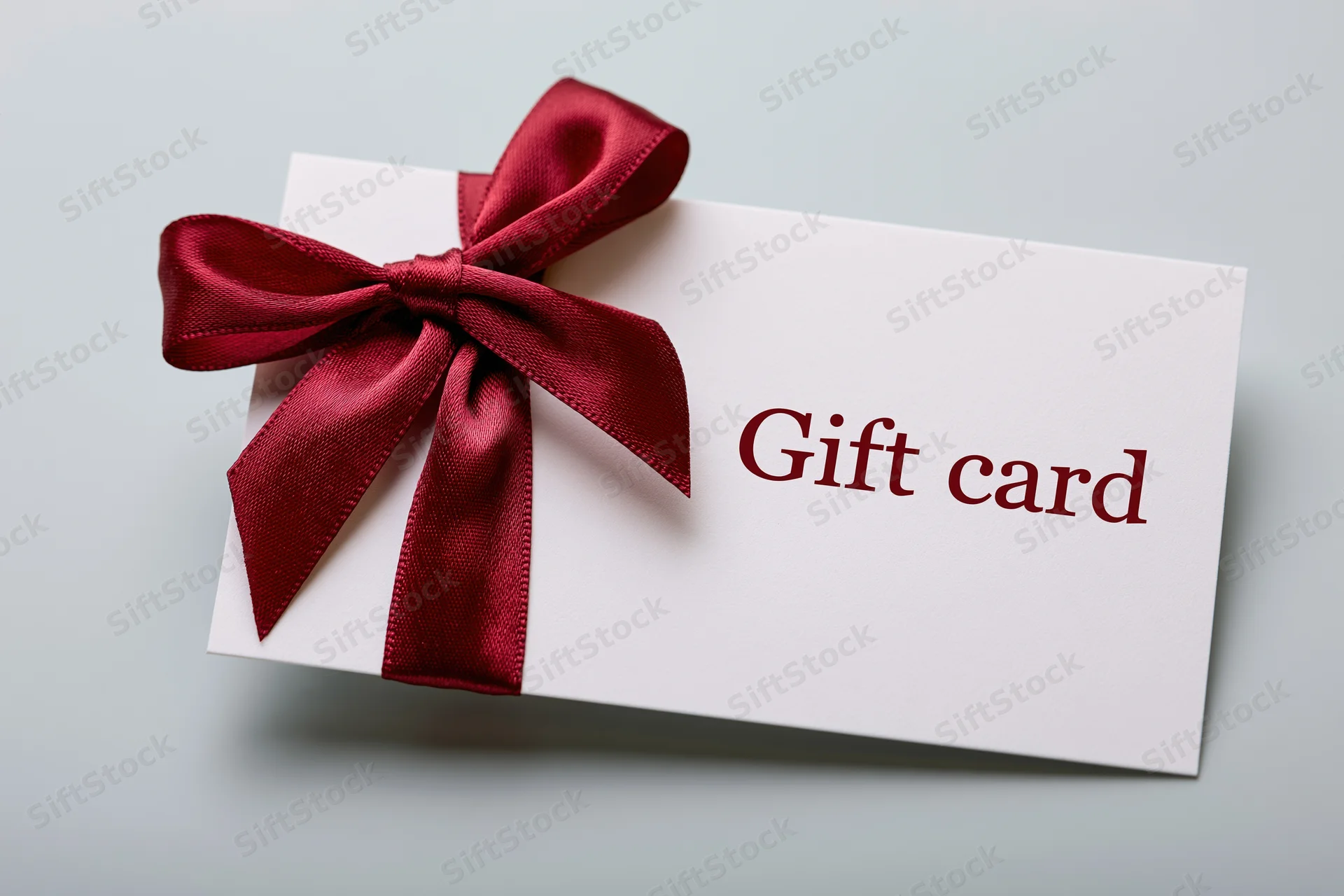 White gift card with red satin bow and printed text lying flat on light surface