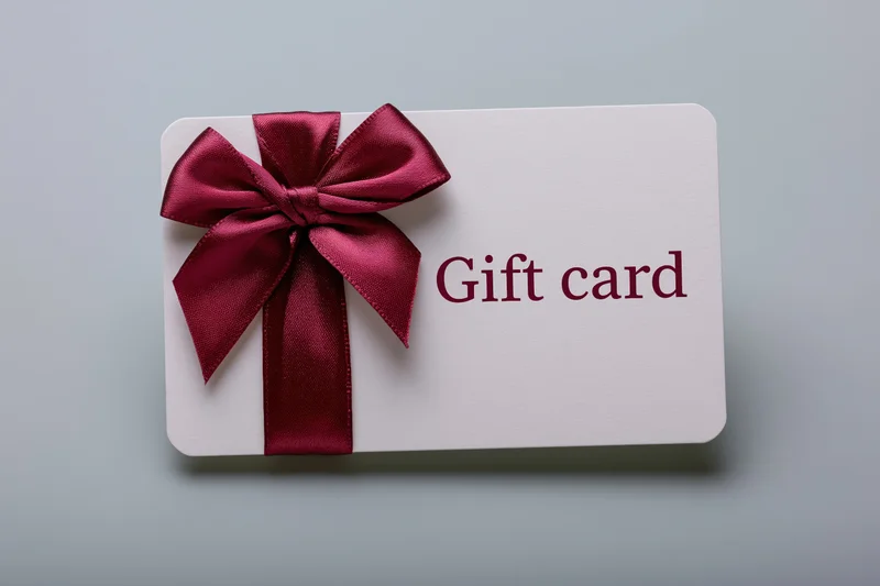 White gift card with burgundy ribbon bow lying flat on light surface