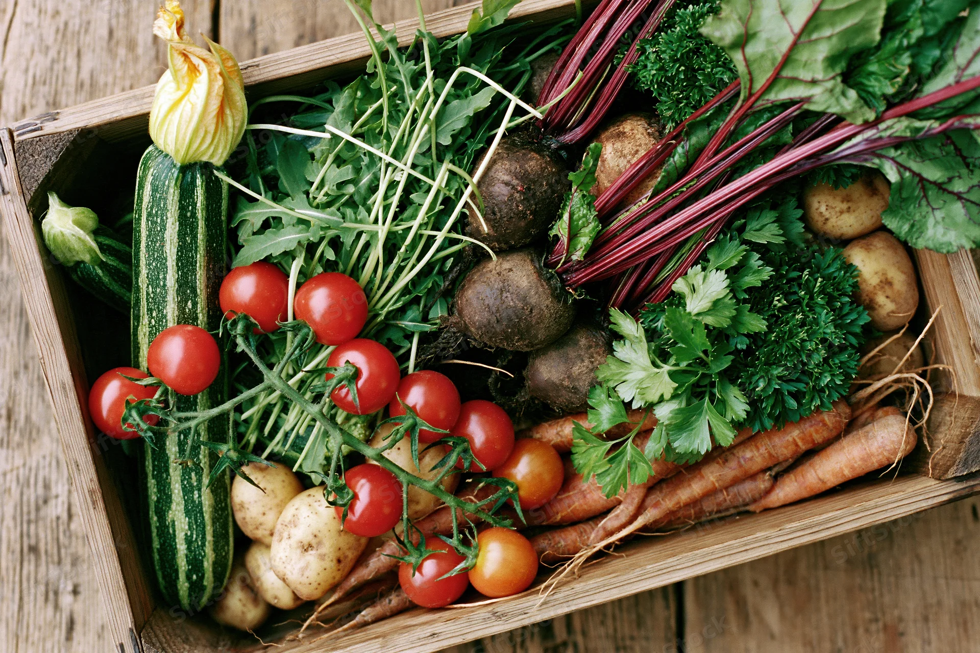 Wooden crate filled with fresh harvested vegetables arranged on rustic surface