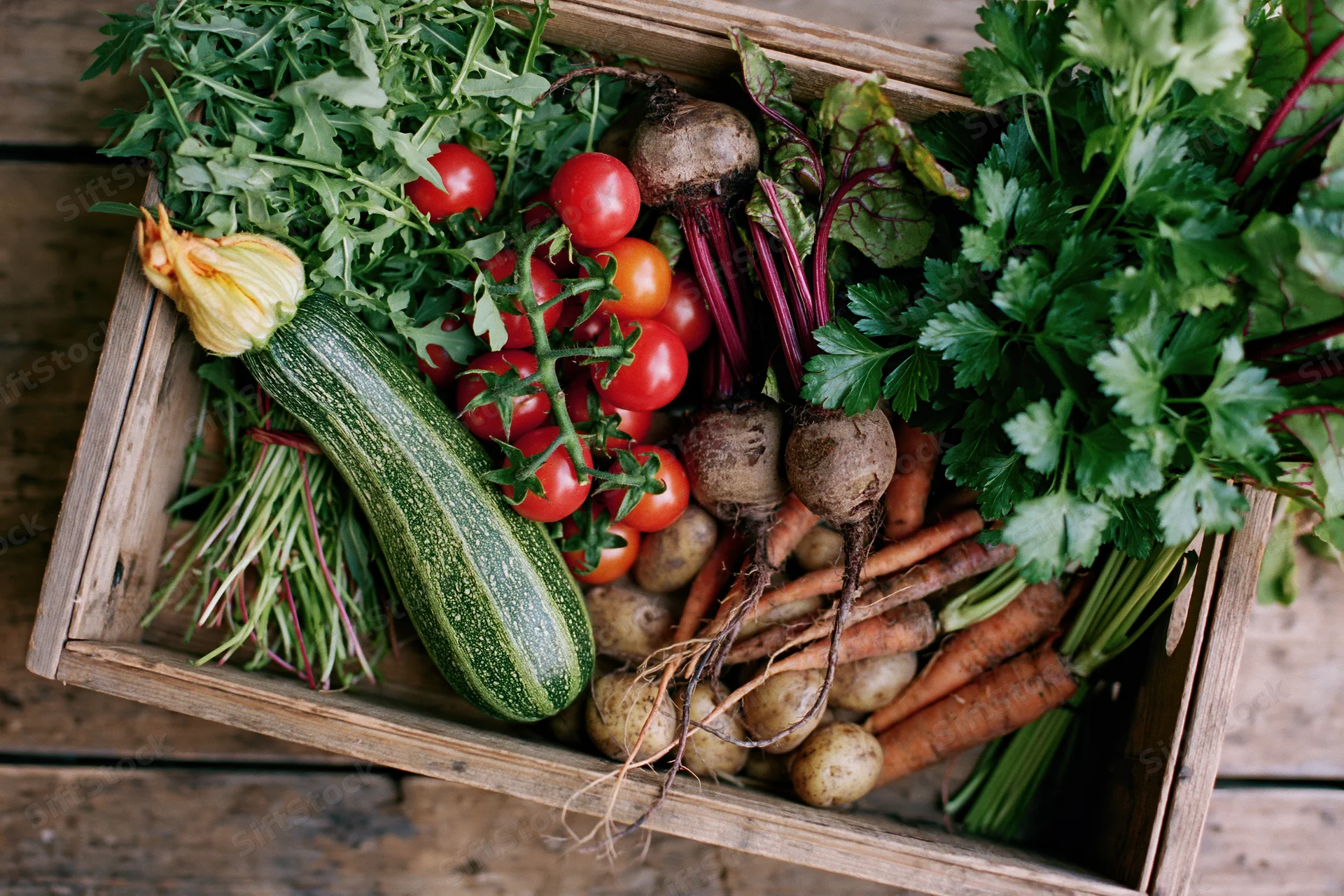 Wooden crate filled with fresh harvested vegetables on rustic wooden surface