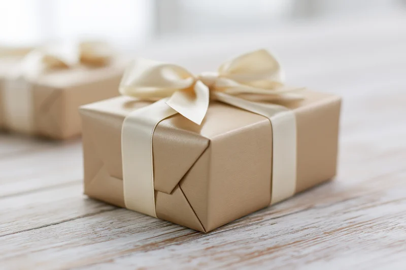 Wrapped gift box in gold paper with cream ribbon bow on wooden surface