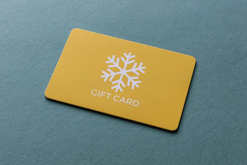 Yellow gift card with white snowflake design lying flat on textured teal surface
