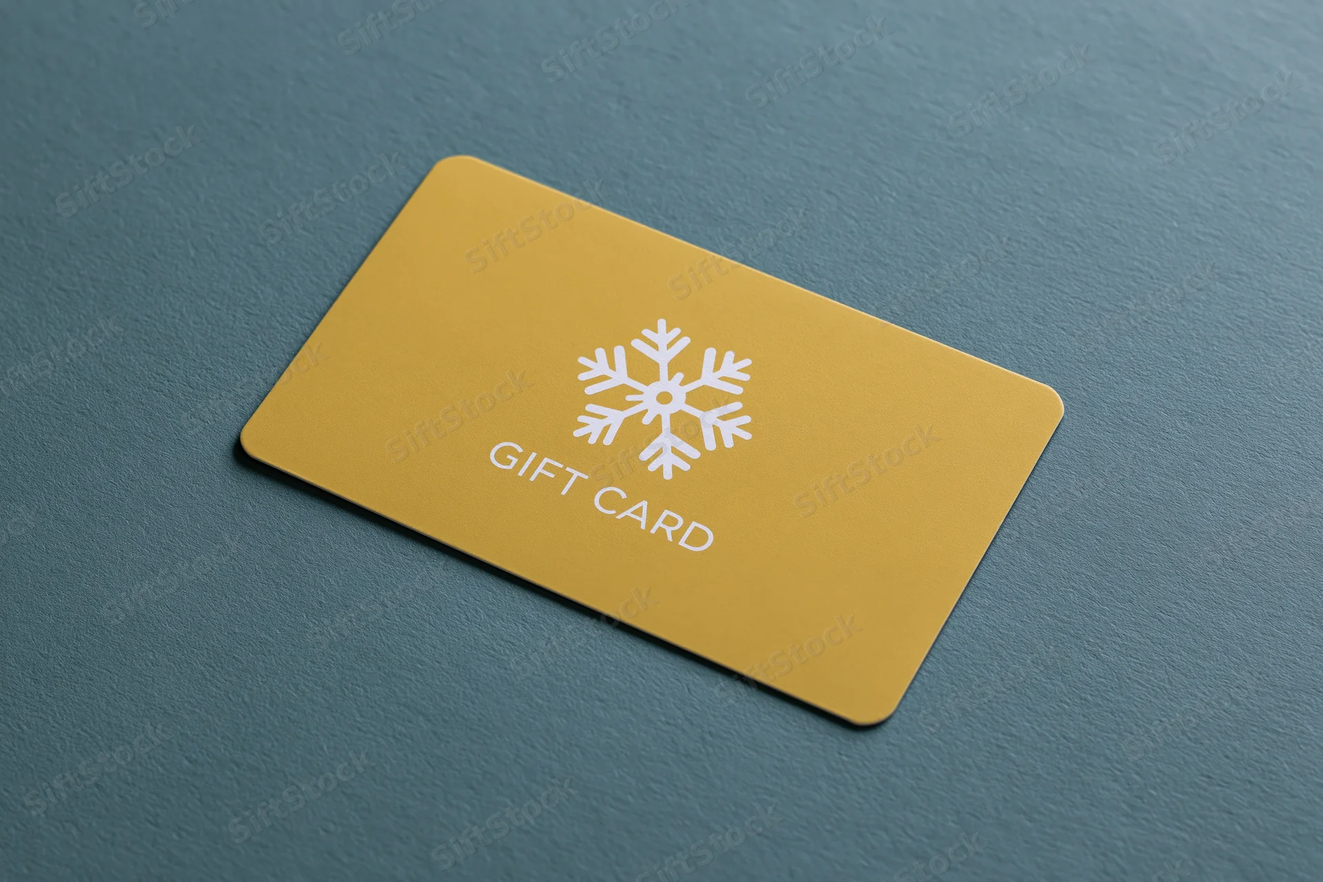 Yellow gift card with snowflake design lying flat on textured teal surface