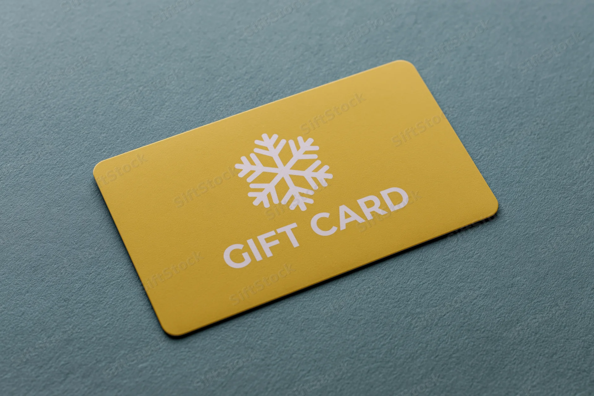 Yellow gift card with snowflake design lying flat on textured teal surface