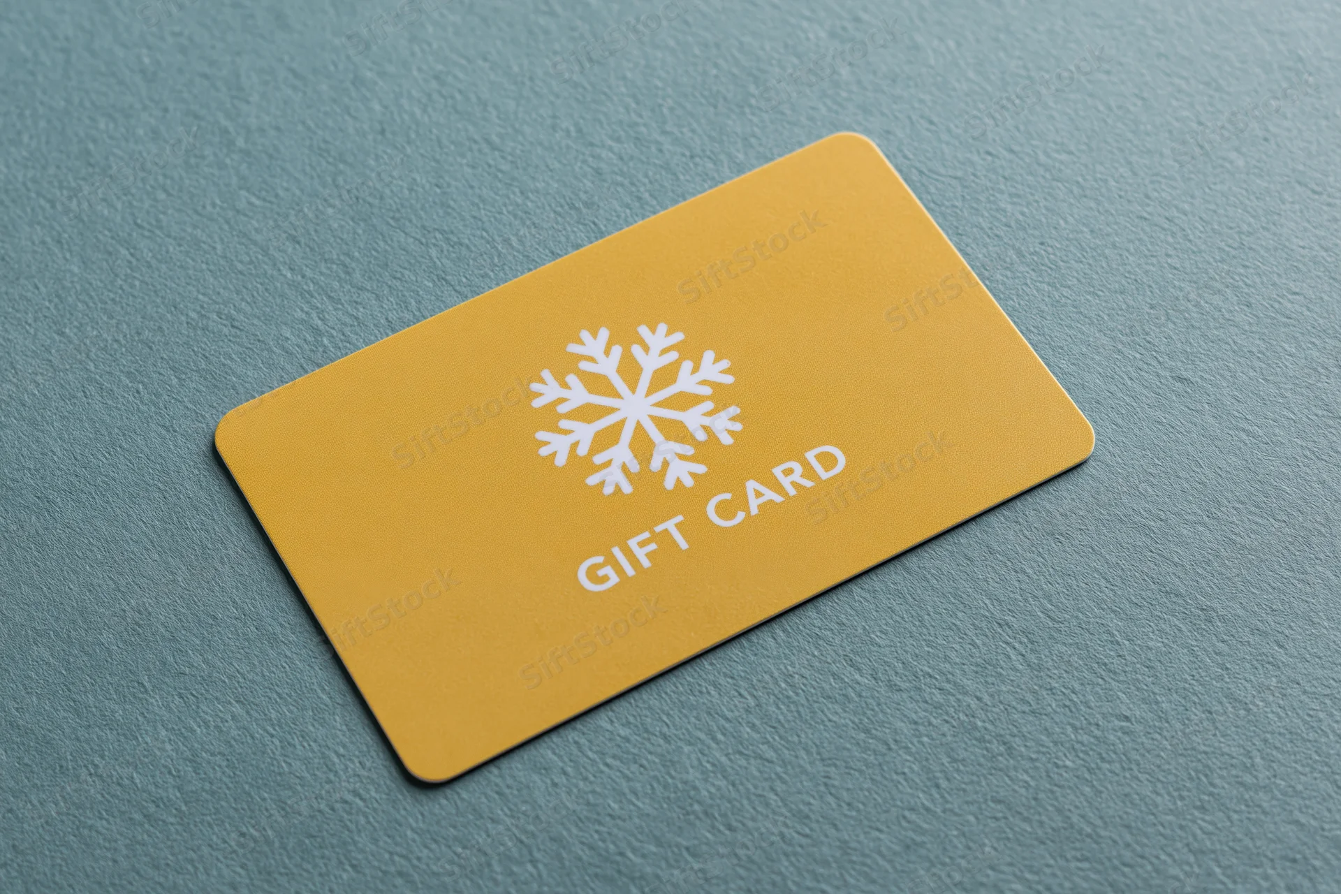 Yellow gift card with snowflake design lying flat on textured teal surface