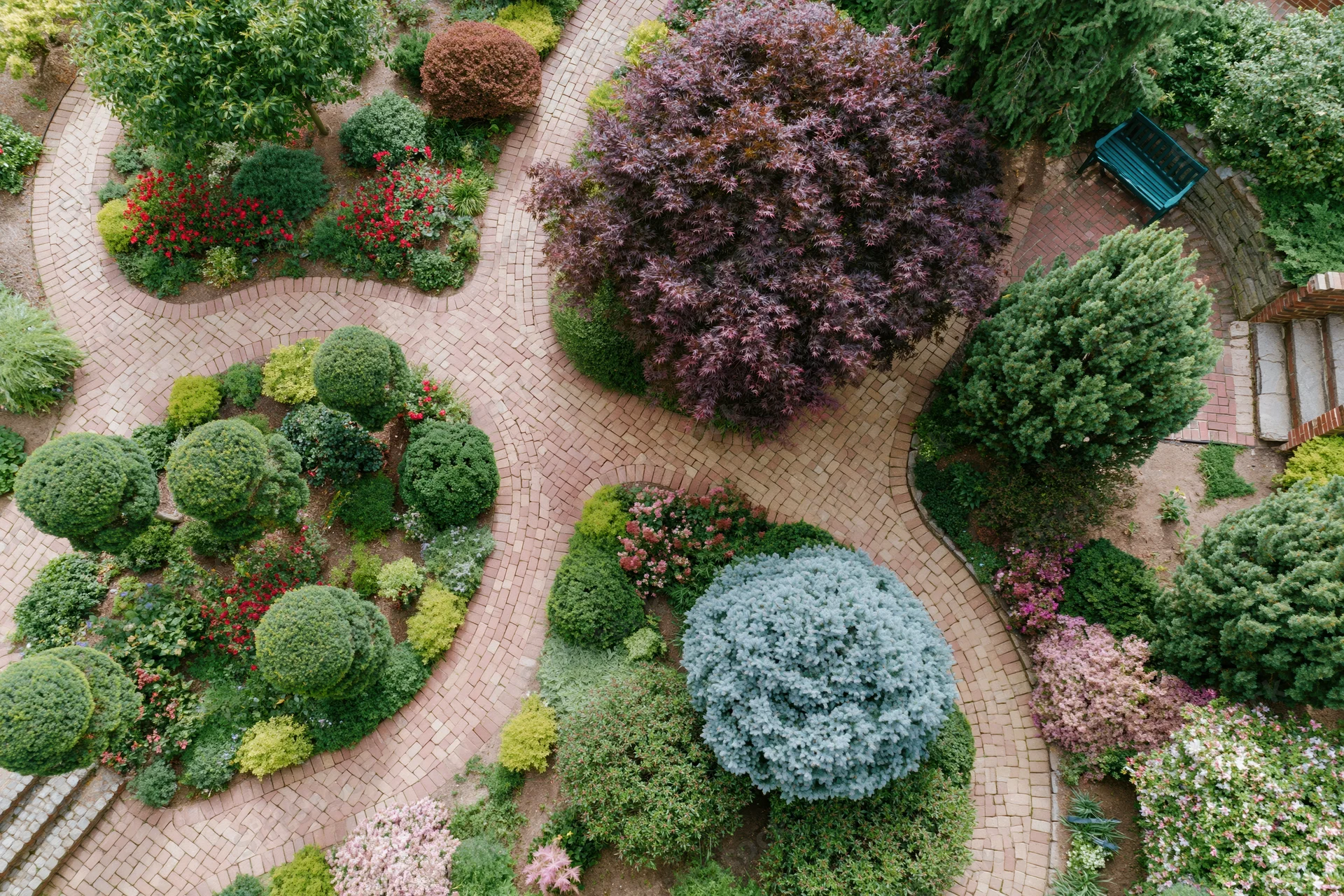 Aerial view of a landscaped garden with topiary shrubs and brick pathways winding through flowering plants and trees