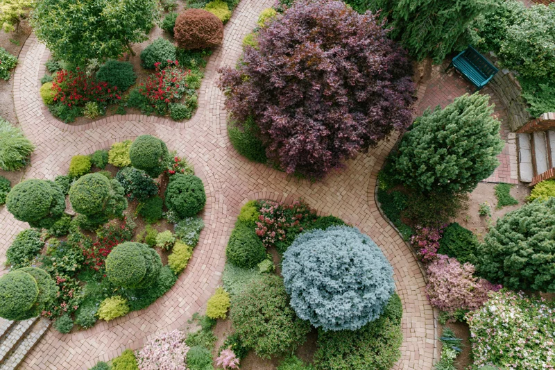 Aerial view of a landscaped garden with topiary shrubs and brick pathways winding through flowering plants and trees