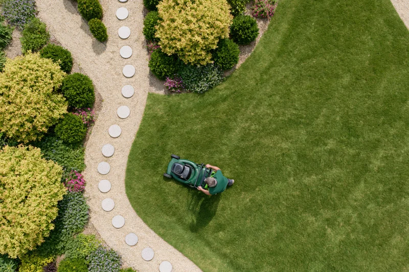 Man mowing a green lawn in a landscaped garden with stone path and shrubs