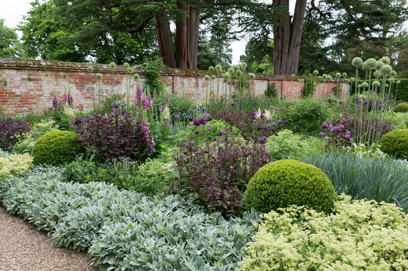 Dense summer garden border with colorful flowers and shrubs along a brick wall