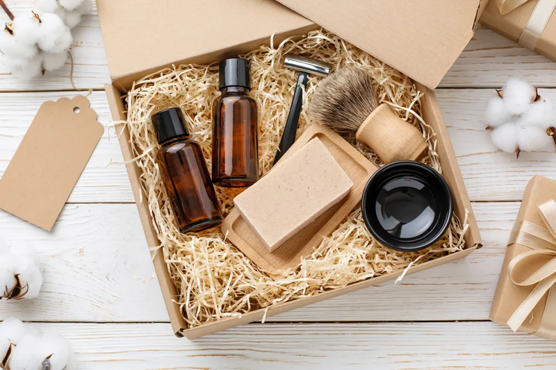 Open gift box with shaving kit and natural grooming products on wooden surface