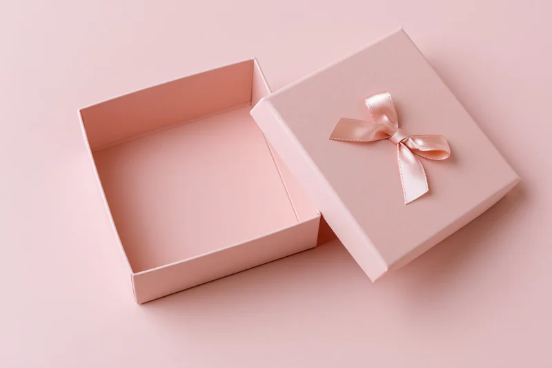 Open square pink gift box with lid and ribbon on matching surface