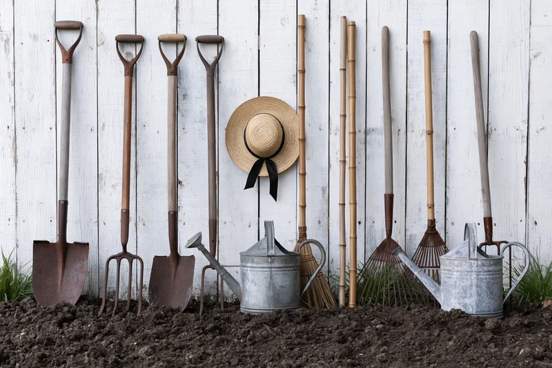 Garden tools arranged against a white wooden wall with soil in front