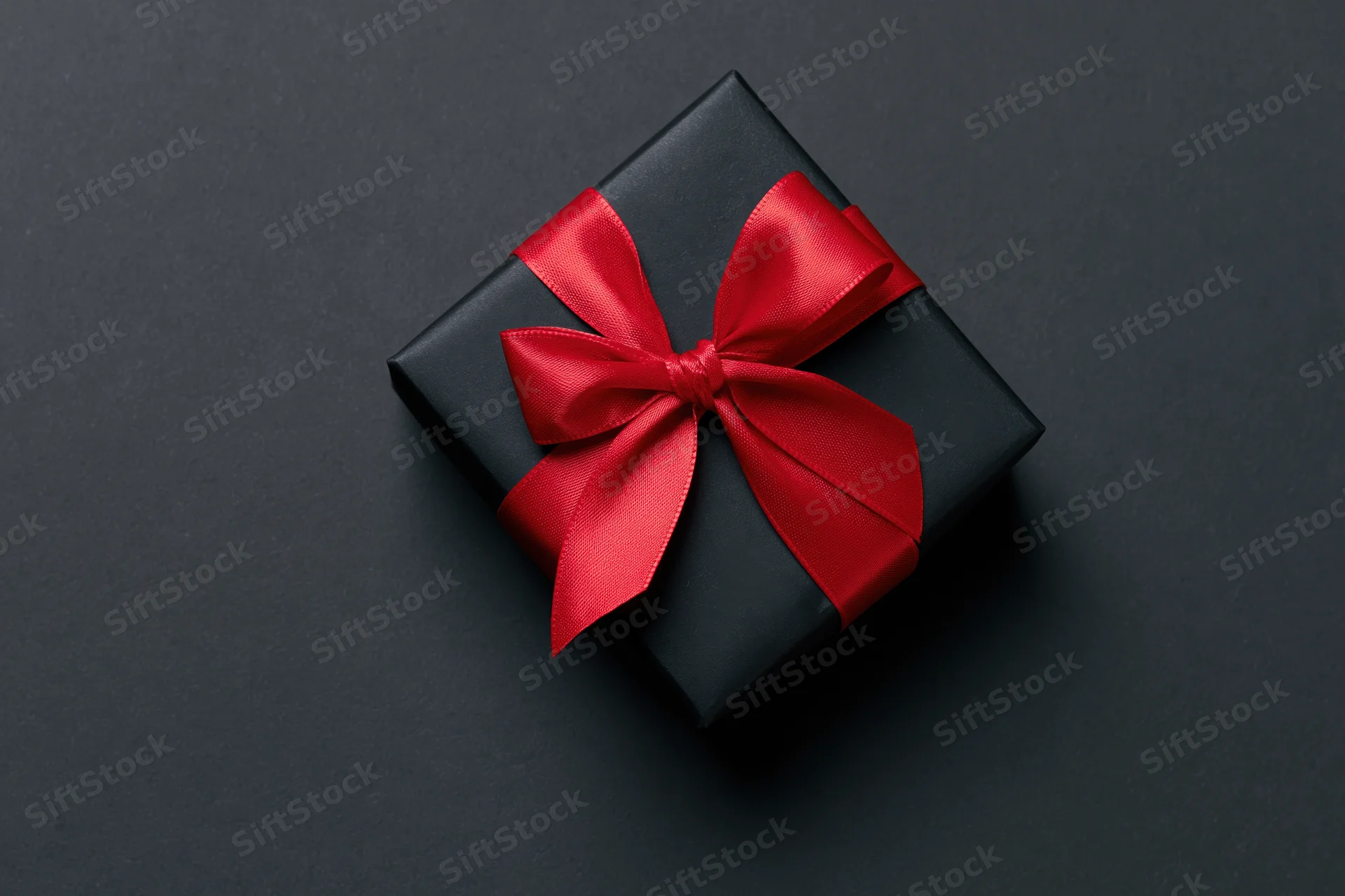 Black gift box with red ribbon bow on dark surface