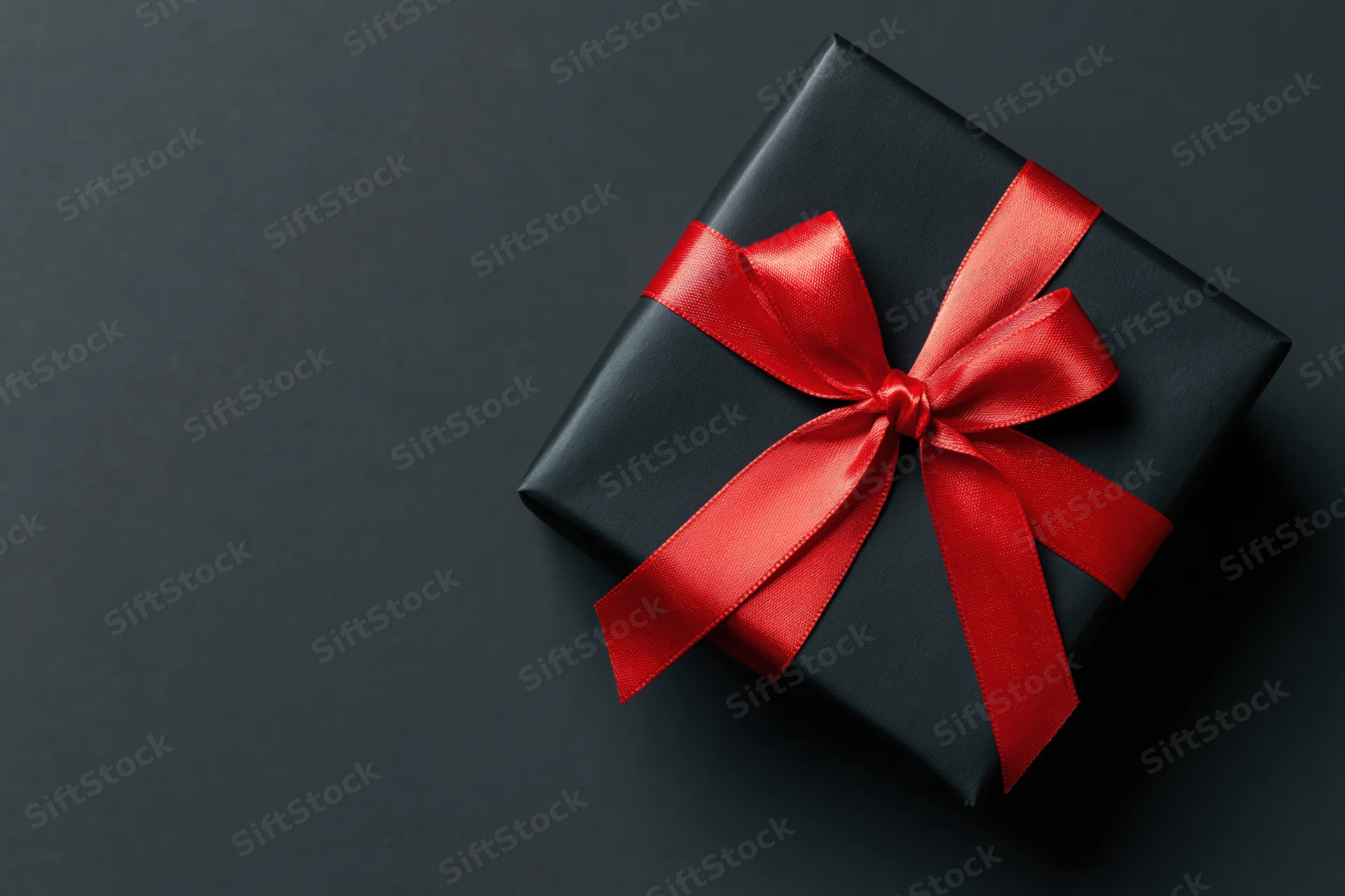 Black gift box wrapped in matte paper with red satin ribbon on dark surface