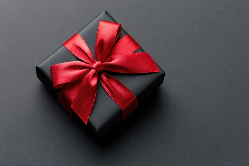 Black gift box wrapped in matte paper with red satin bow on dark surface