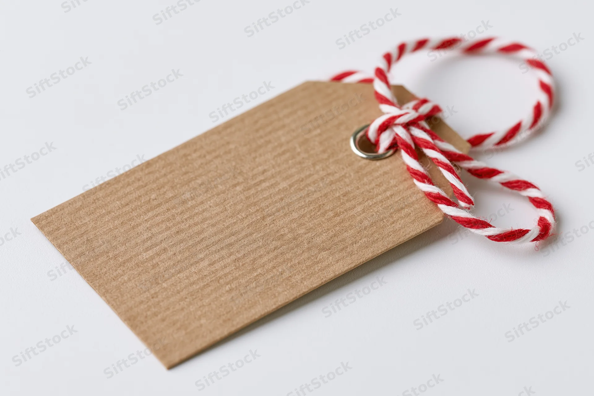 Blank kraft paper gift tag with red and white twine tied in a bow on white background