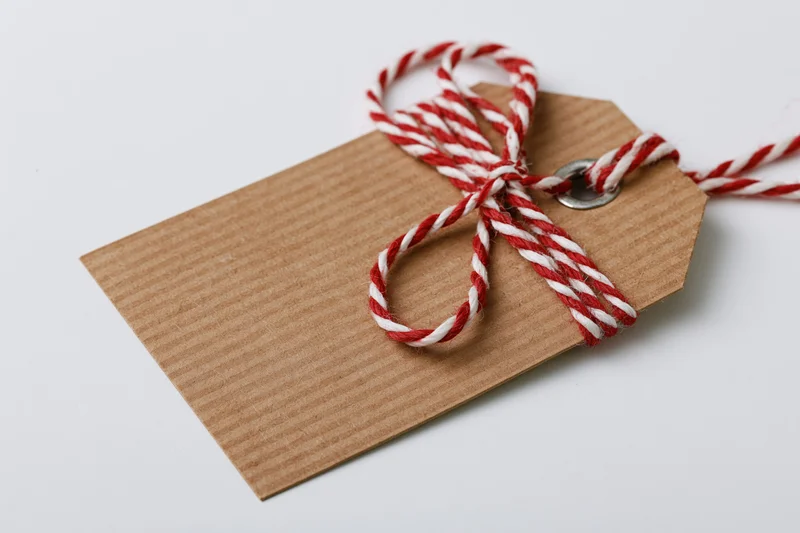 Blank kraft paper gift tag tied with red and white twine bow on white background