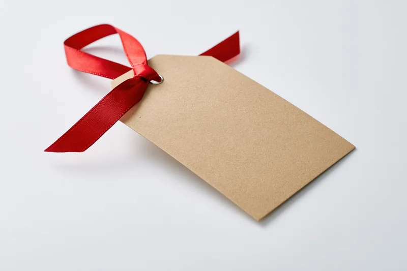 Blank kraft paper gift tag with red satin ribbon tied in a bow on white background