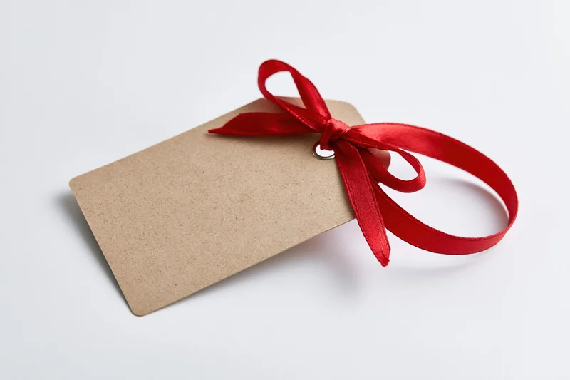 Blank kraft paper gift tag with red satin ribbon tied in a bow on white background