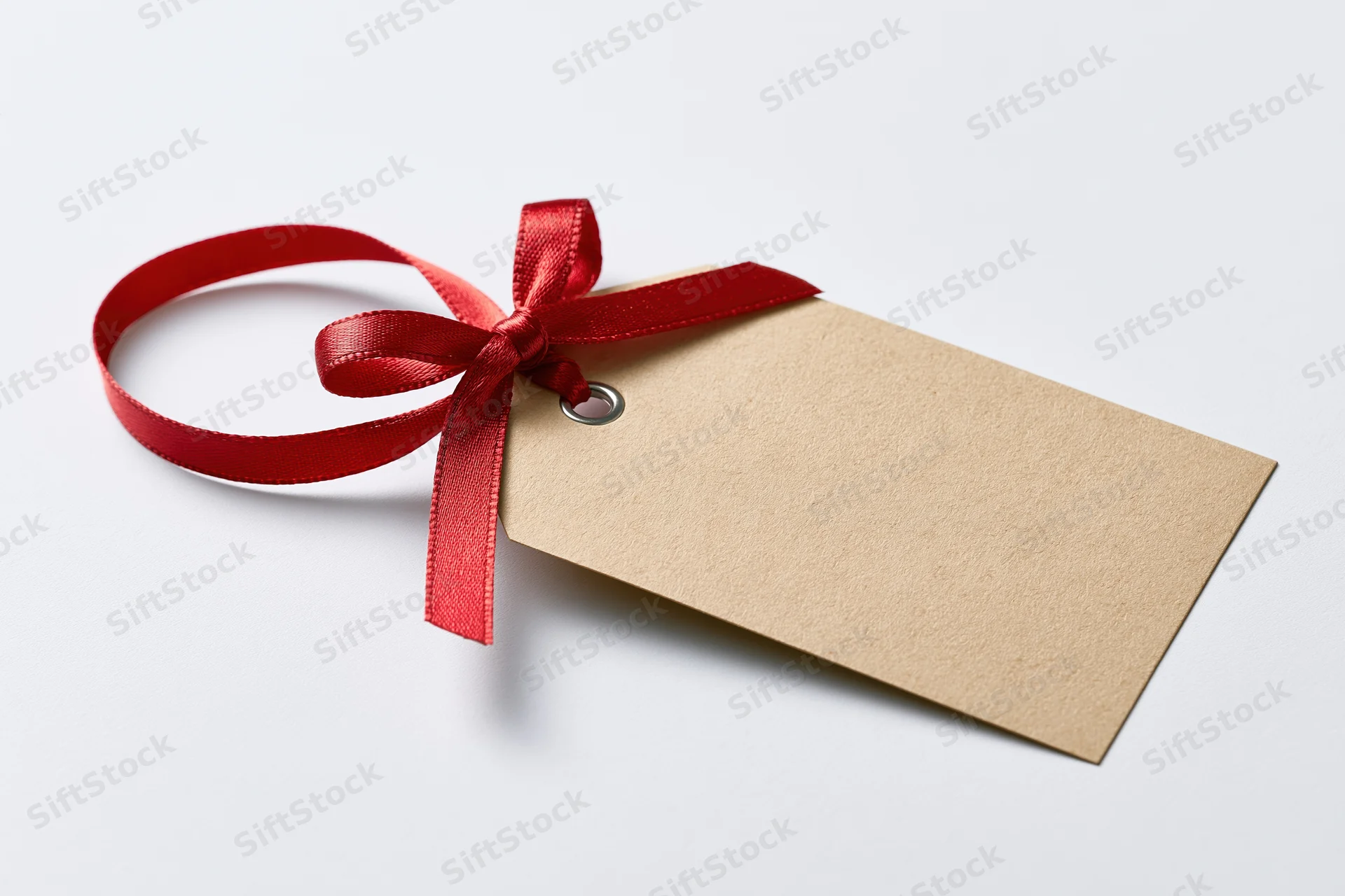 Blank kraft paper gift tag with red satin ribbon tied in a bow on white background